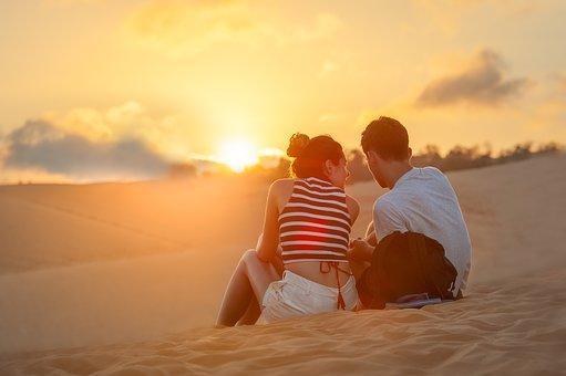 a couple is sitting together on sand during sunset